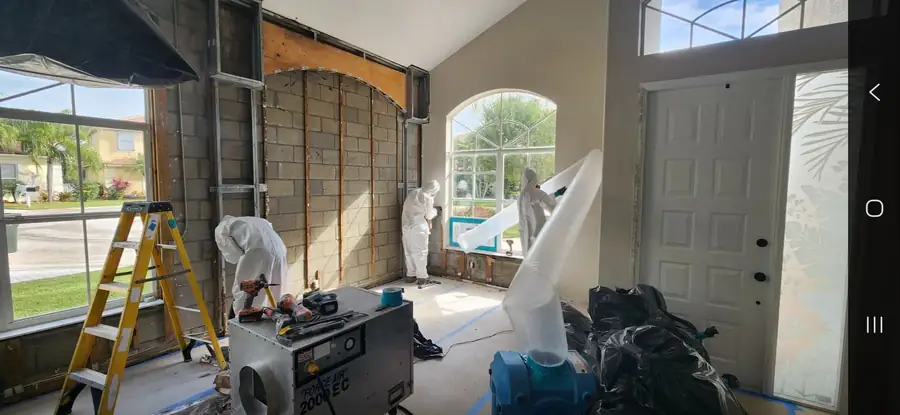 Restoration crew in protective suits working around exposed walls and containment equipment